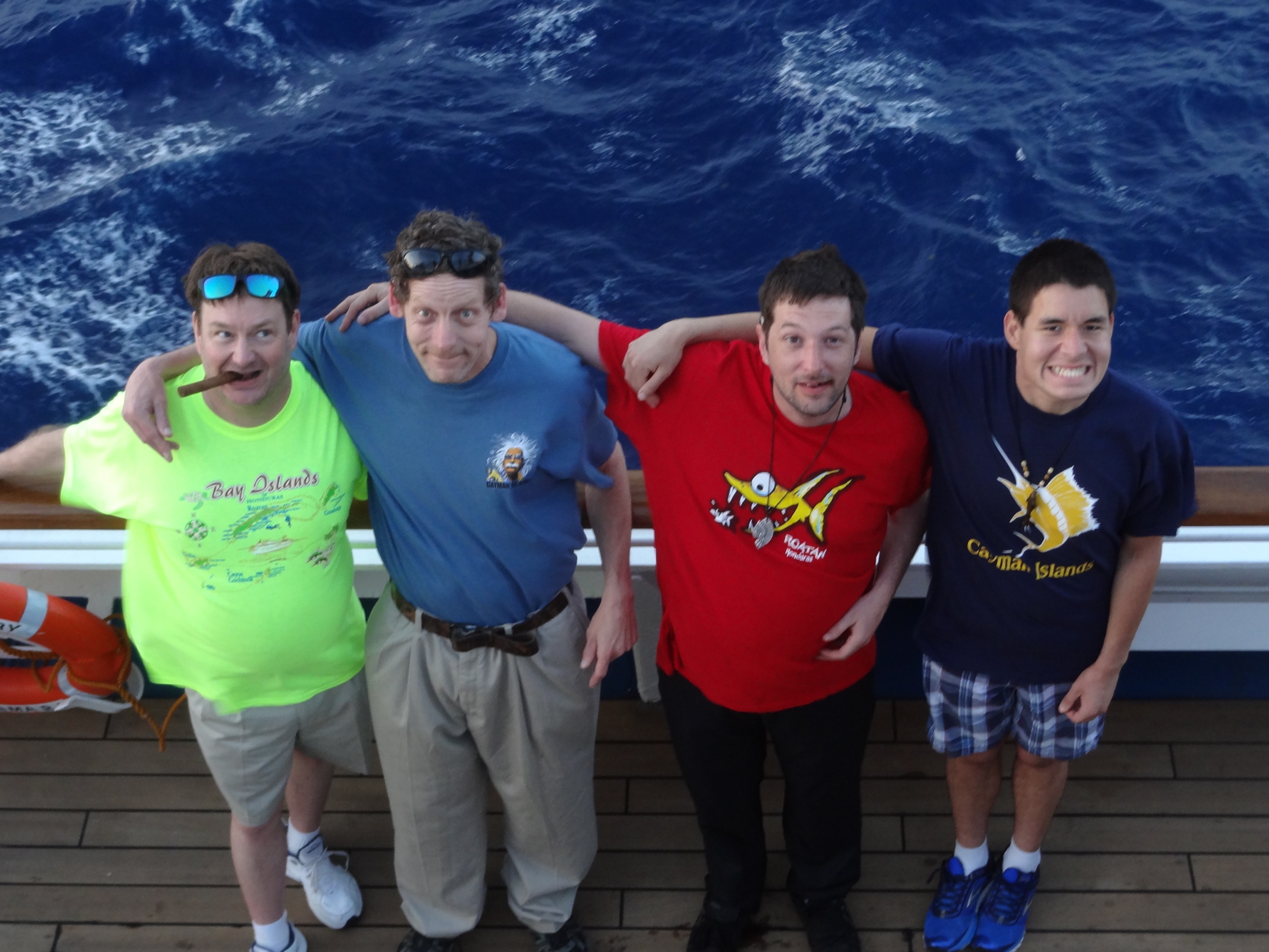 four men with arms around each other smiling for a photo on a ship