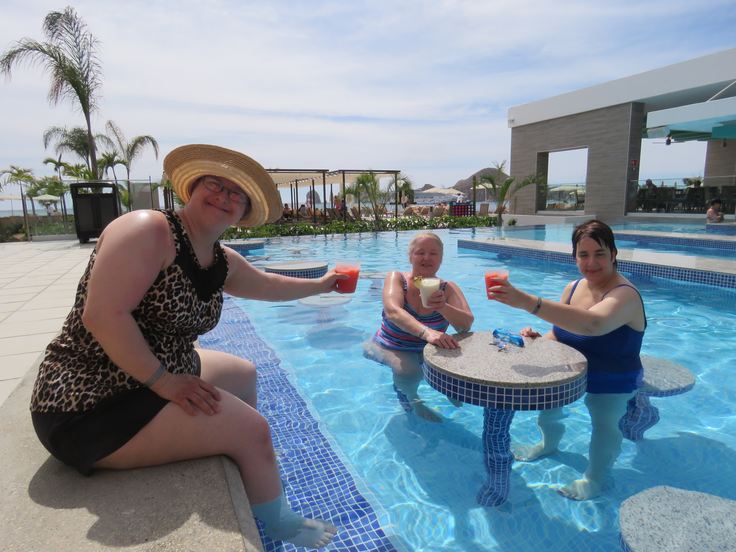 three women doing a cheers with drinks in a pool
